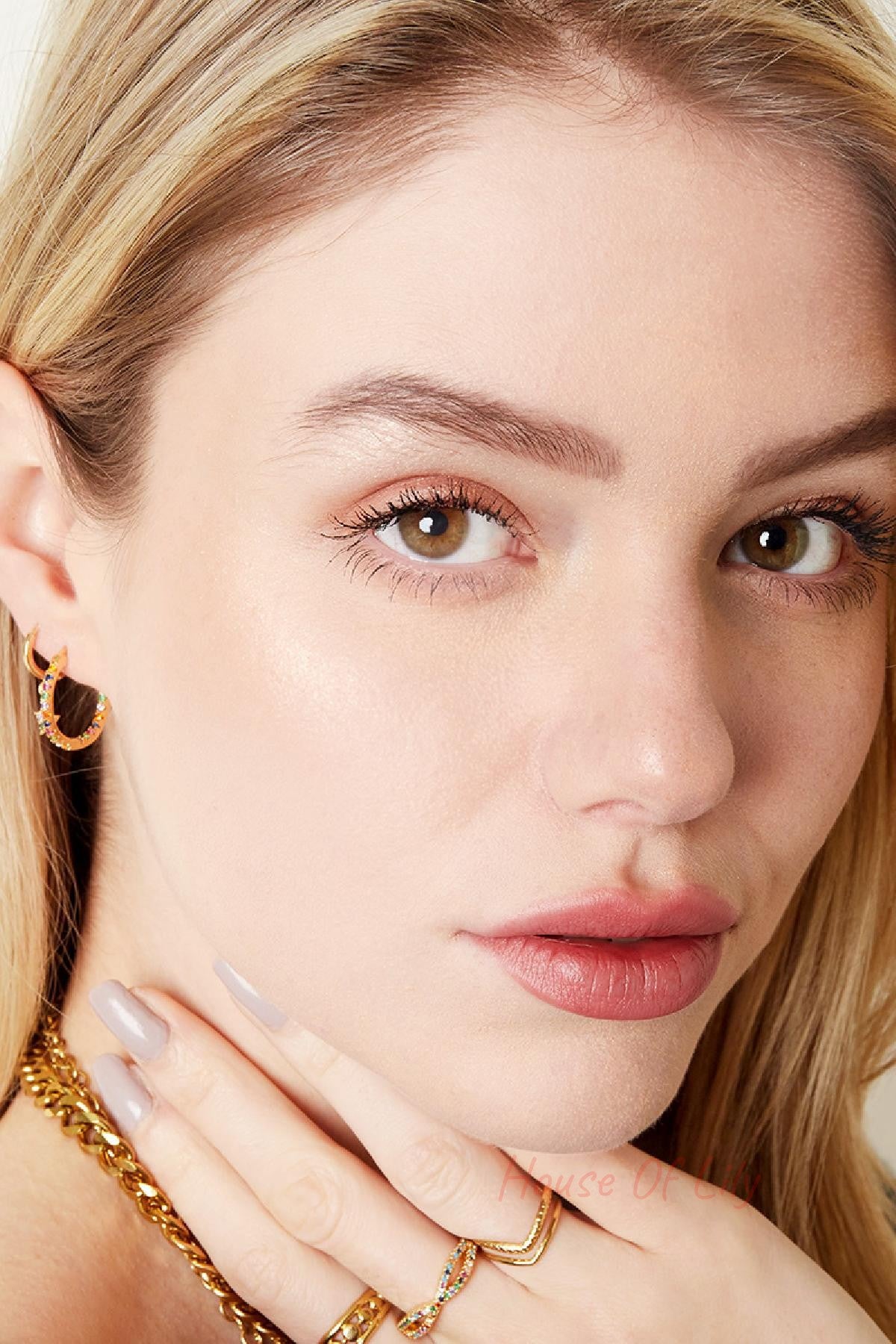 Close-up of woman wearing colorful stone hoop earrings with matching gold rings and necklace