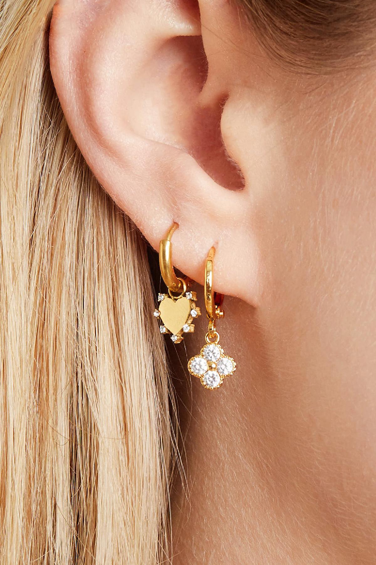 Close-up side view of a woman’s ear adorned with gold clover and heart charm earrings