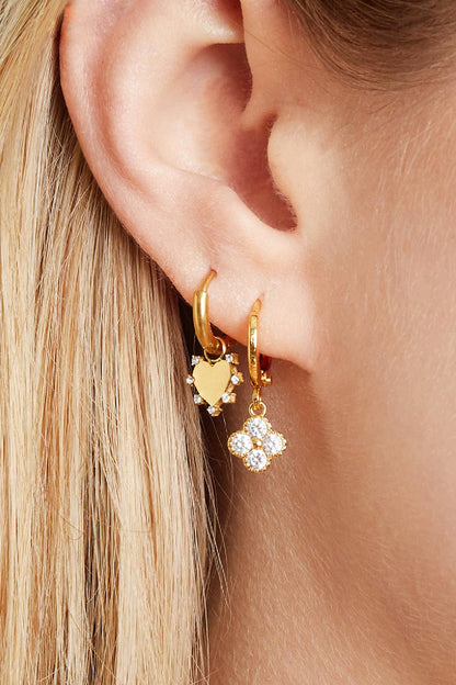 Close-up side view of a woman’s ear adorned with gold clover and heart charm earrings