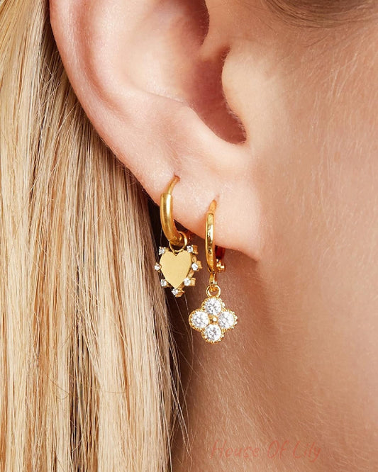 Close-up side view of a woman’s ear adorned with gold clover and heart charm earrings