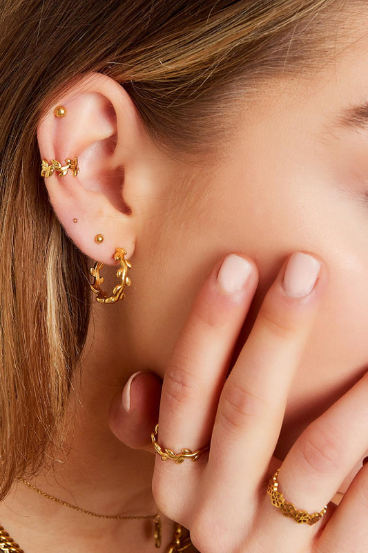 Model wearing gold laurel leaf earcuff, matching ring, and hoop earrings with youthful styled hair and nails