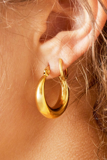 Extreme close-up of chunky gold hoop earring worn on ear showcasing smooth curves and polished shine
