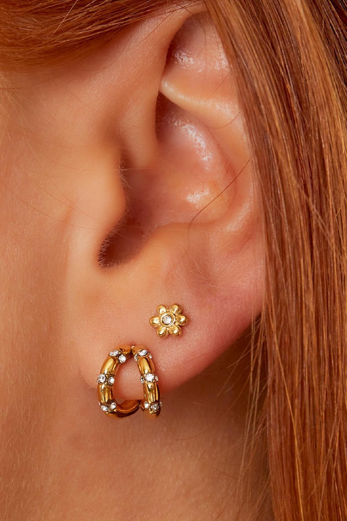 Close-up of ear wearing gold floral mini stud earring paired with gold hoop earrings with rhinestones