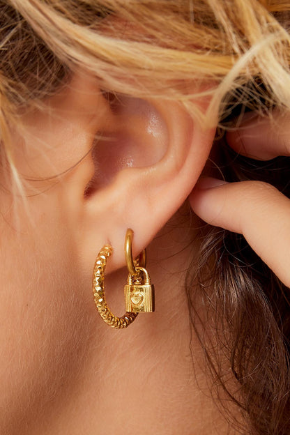 Close-up of gold textured hoop earrings worn with an additional small gold hoop earring featuring a small padlock charm