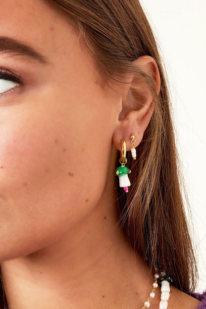 Close-up of ear with multiple earrings including gold-tone drop earring with freshwater pearl and a green mushroom charm earring