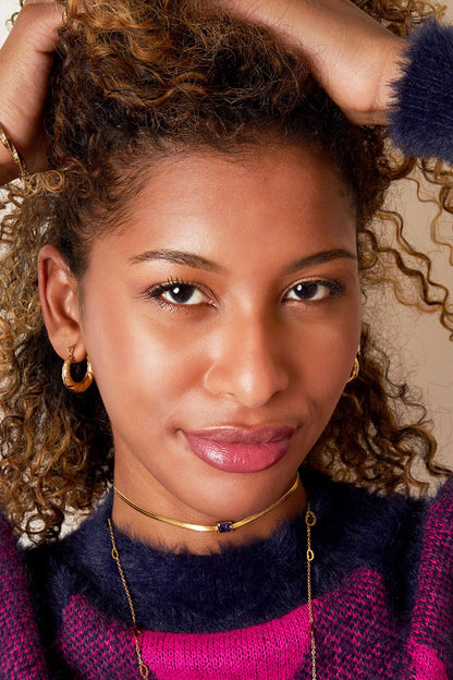 Close-up portrait of woman wearing braided gold hoop earrings, smiling with curly hair