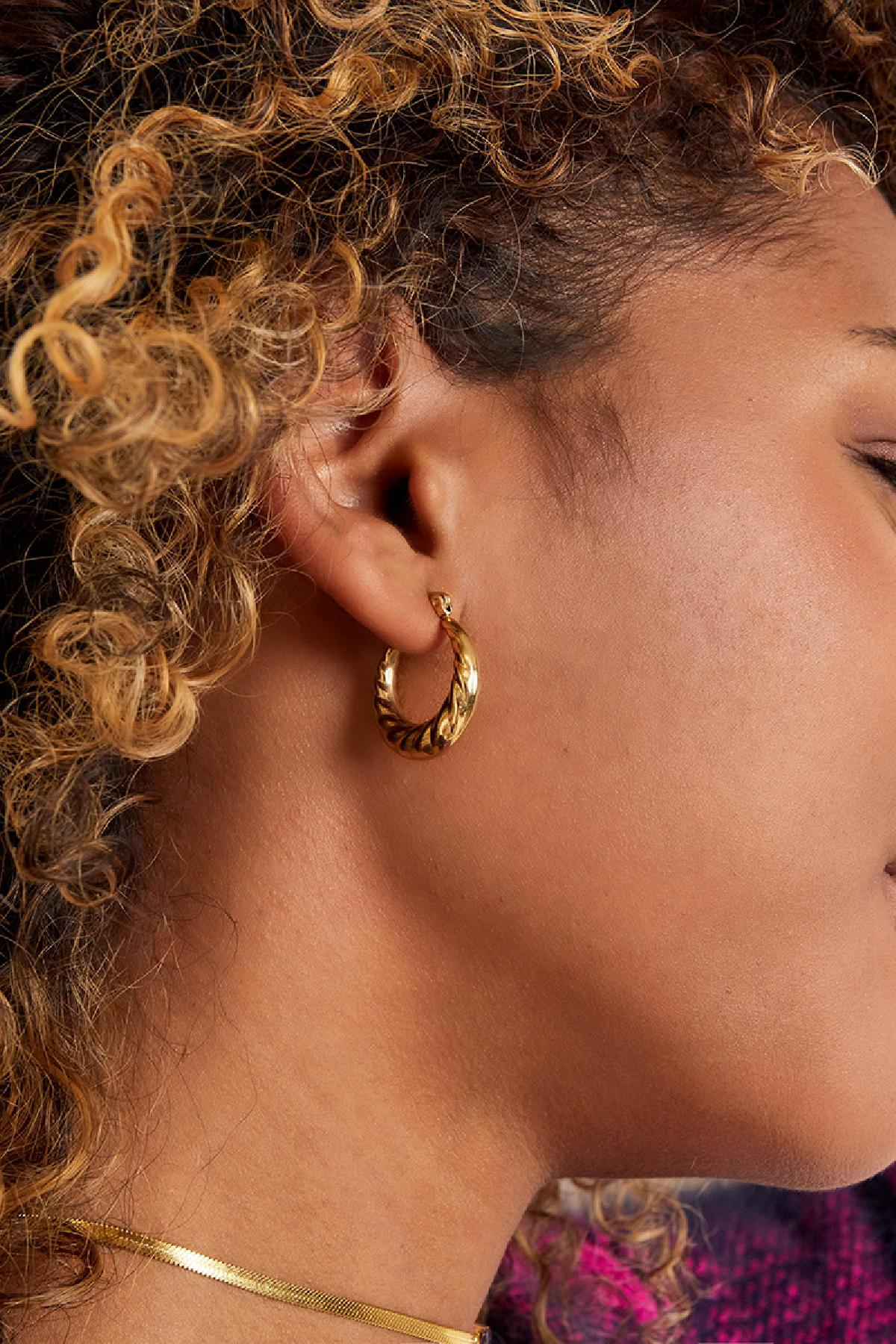 Side profile of woman wearing braided gold hoop earrings, showing detailed texture