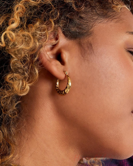 Side profile of woman wearing braided gold hoop earrings, showing detailed texture