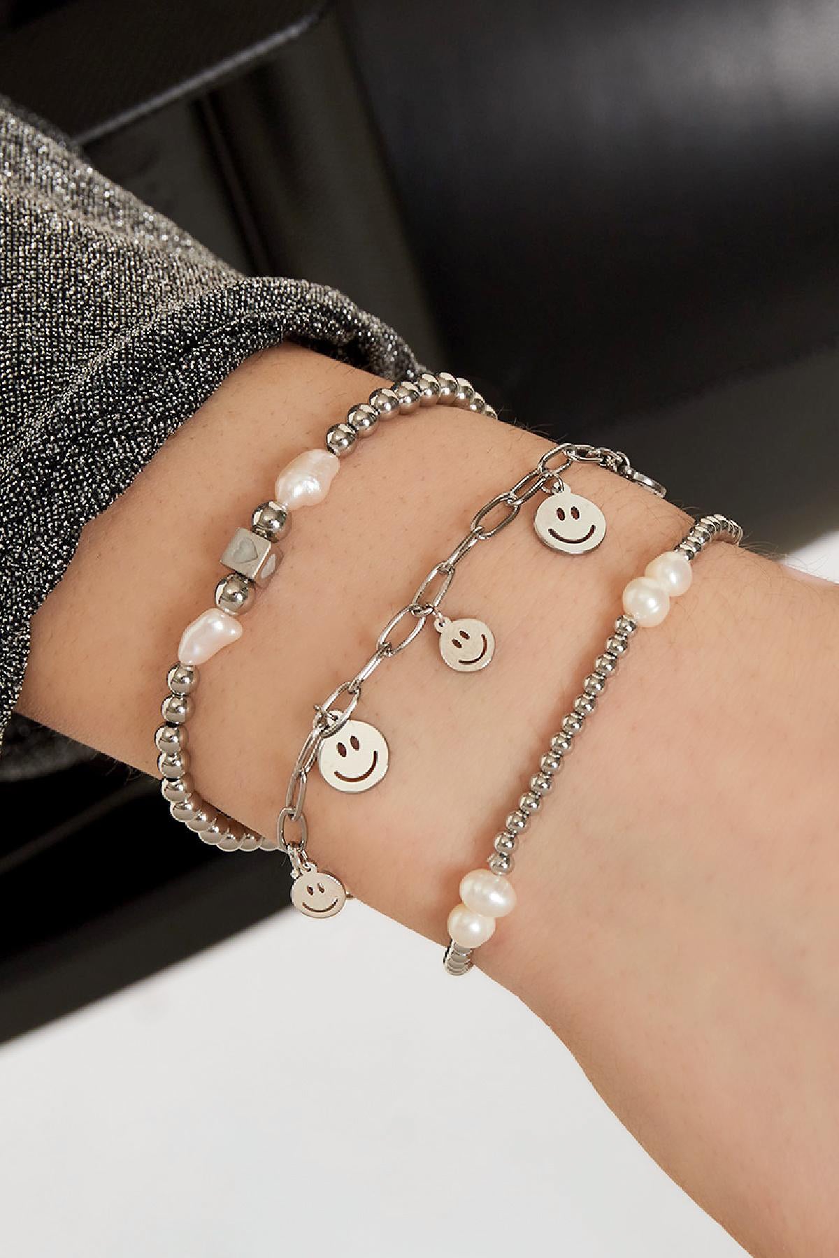 Wrist wearing three bracelets: silver smiley face charm bracelet paired with pearl and silver beaded bracelets