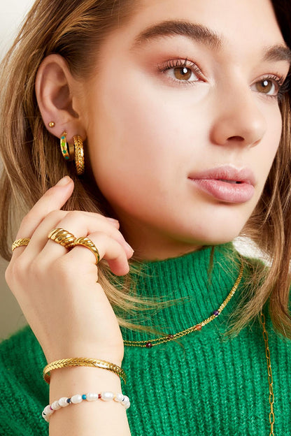 Close-up of woman showing gold laurel cuff bracelet, rings, and layered necklaces on green sweater