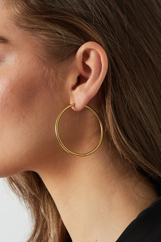 Close-up of woman wearing one large gold hoop earring showing soft and sleek design