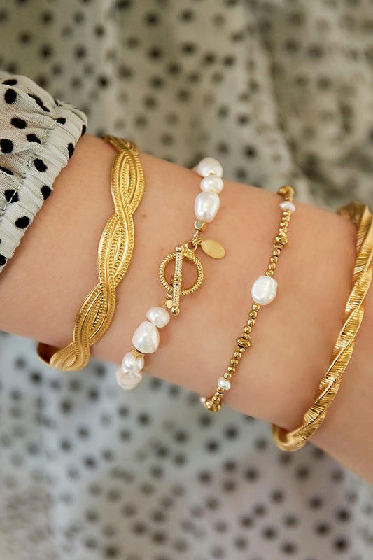 Wrist adorned with stacked bracelets including a pearl beaded bracelet with gold accents against polka dot sleeve