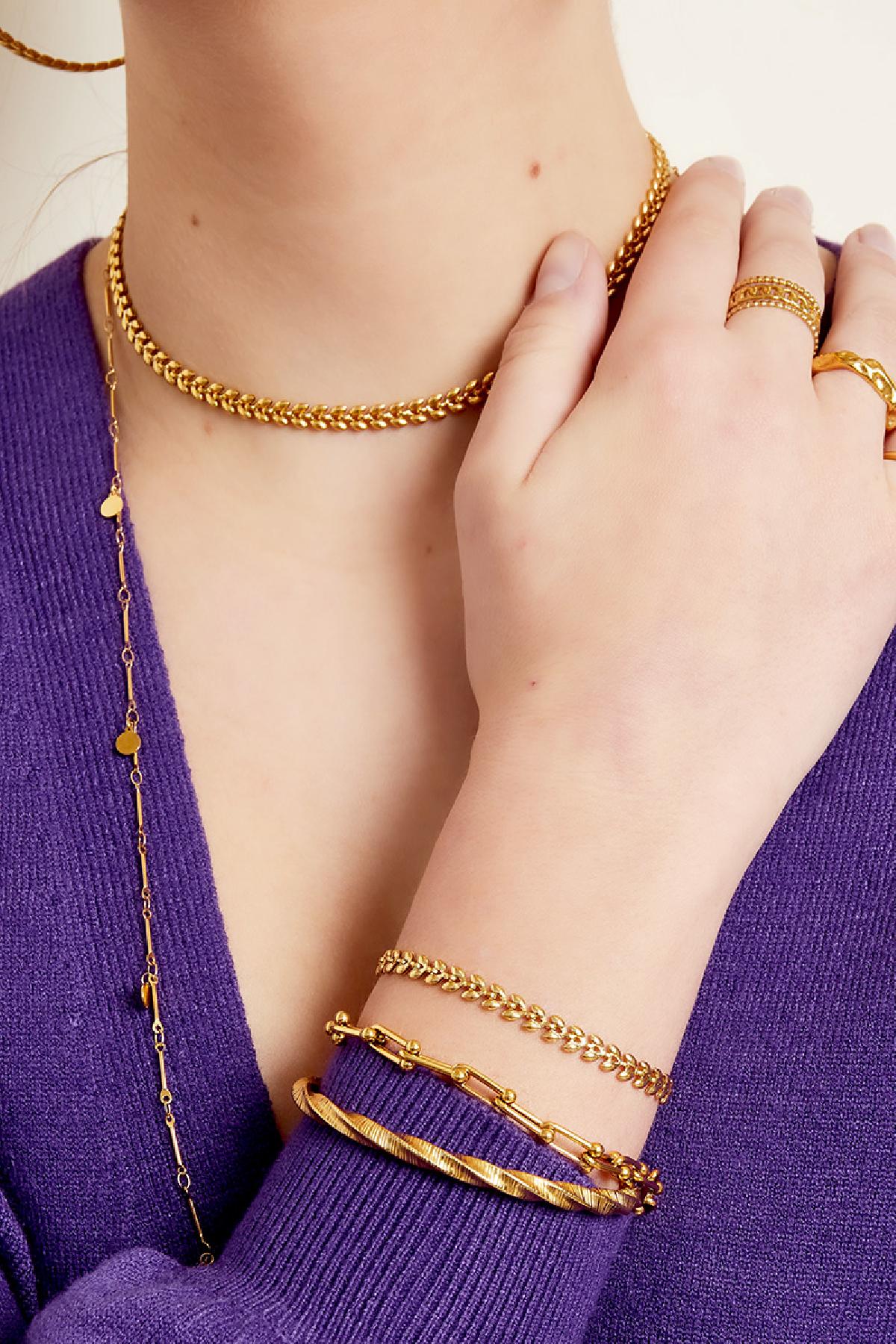 Model wearing gold leaf chain bracelet stacked with other gold bracelets and matching necklace, dressed in purple top