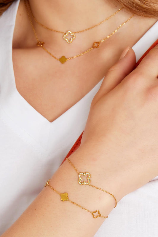 Model wearing layered gold clover charm necklace and matching bracelets with sparkling zircon stones