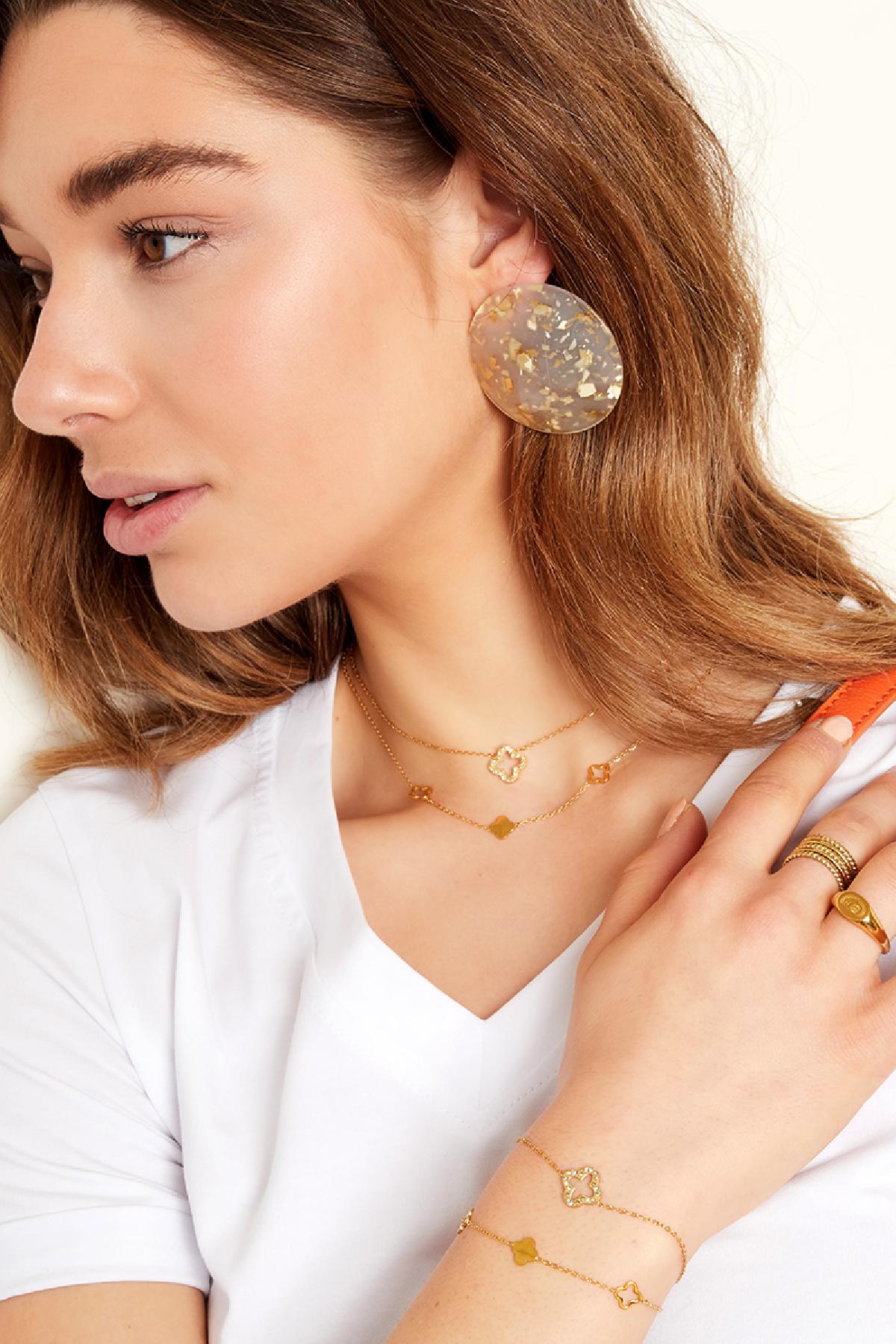 Close-up of a model wearing layered clover charm necklaces and bracelets in gold, paired with statement earrings and rings