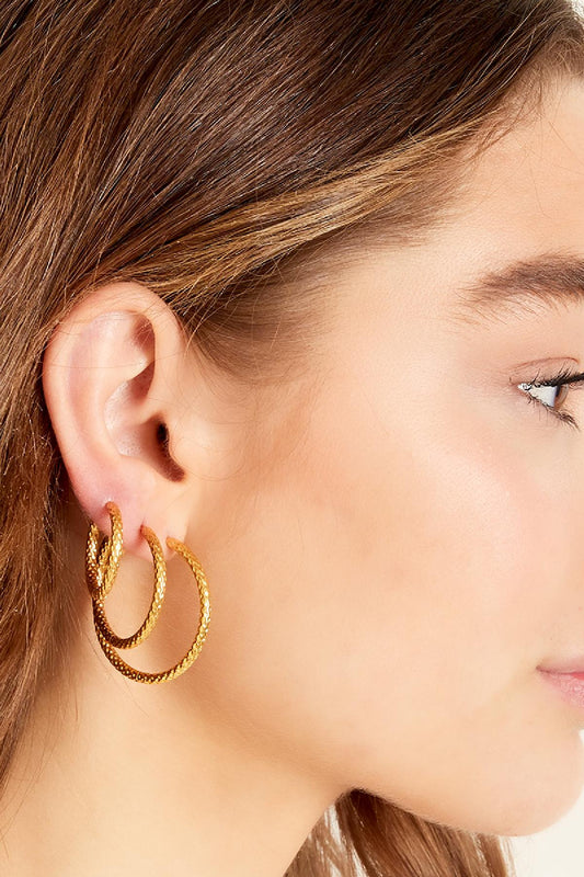 Side profile of woman wearing three sizes of textured gold hoop earrings on left ear