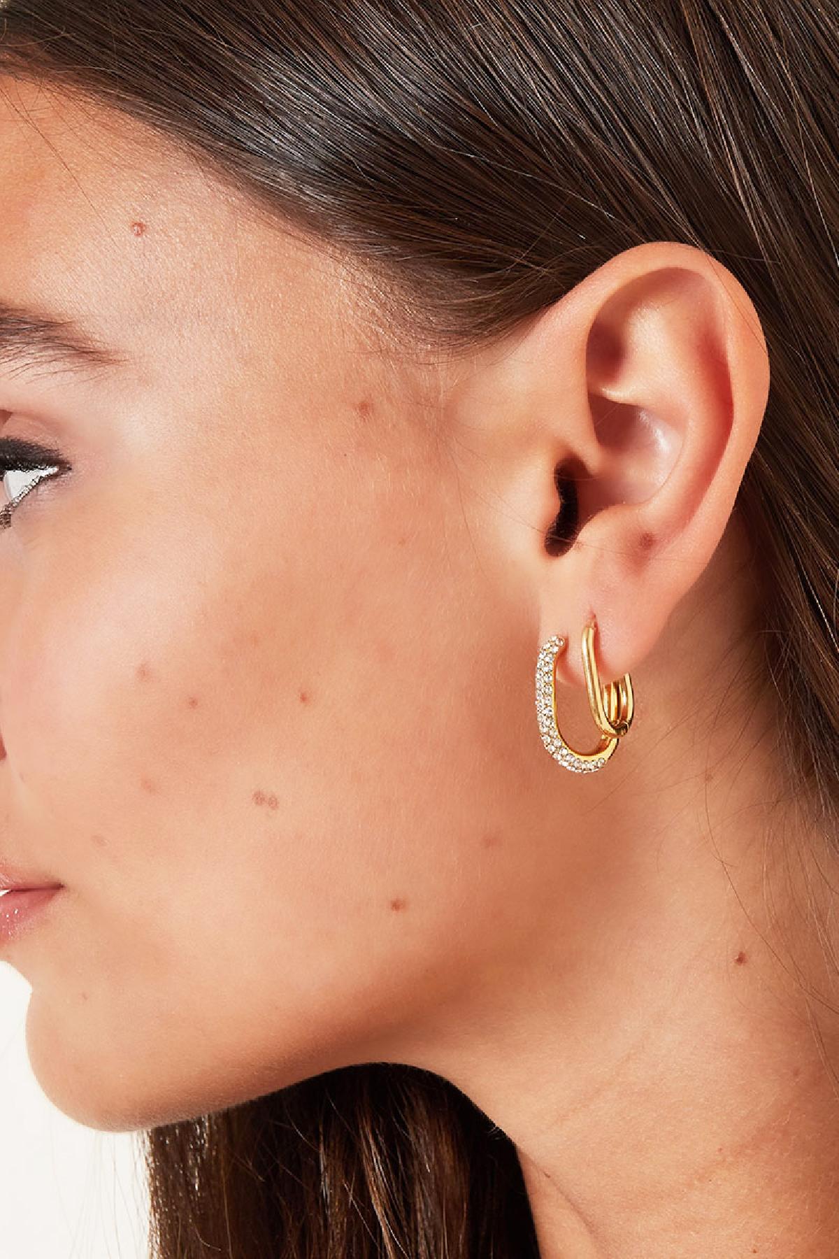 Close-up profile of a woman wearing a gold oval hoop earring paired with a rhinestone-encrusted oval hoop