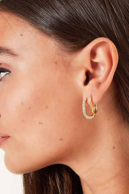 Close-up profile of a woman wearing a gold oval hoop earring paired with a rhinestone-encrusted oval hoop