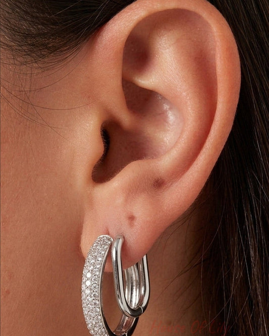 Silver double hoop earrings: one pavé-set with sparkling white stones, the other a smooth, polished oval loop.