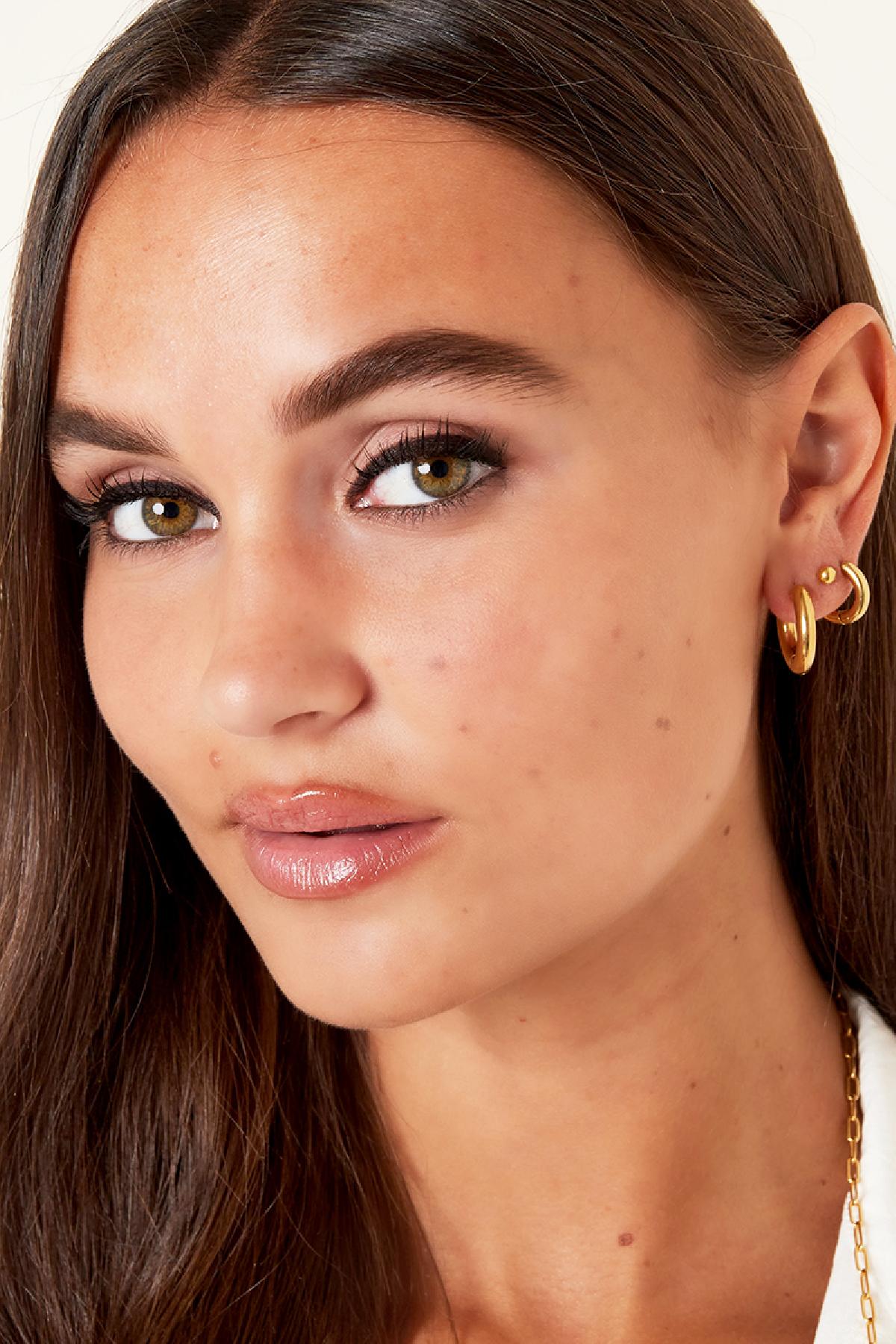 Close-up of female model wearing layered chunky gold hoop earrings and a small stud