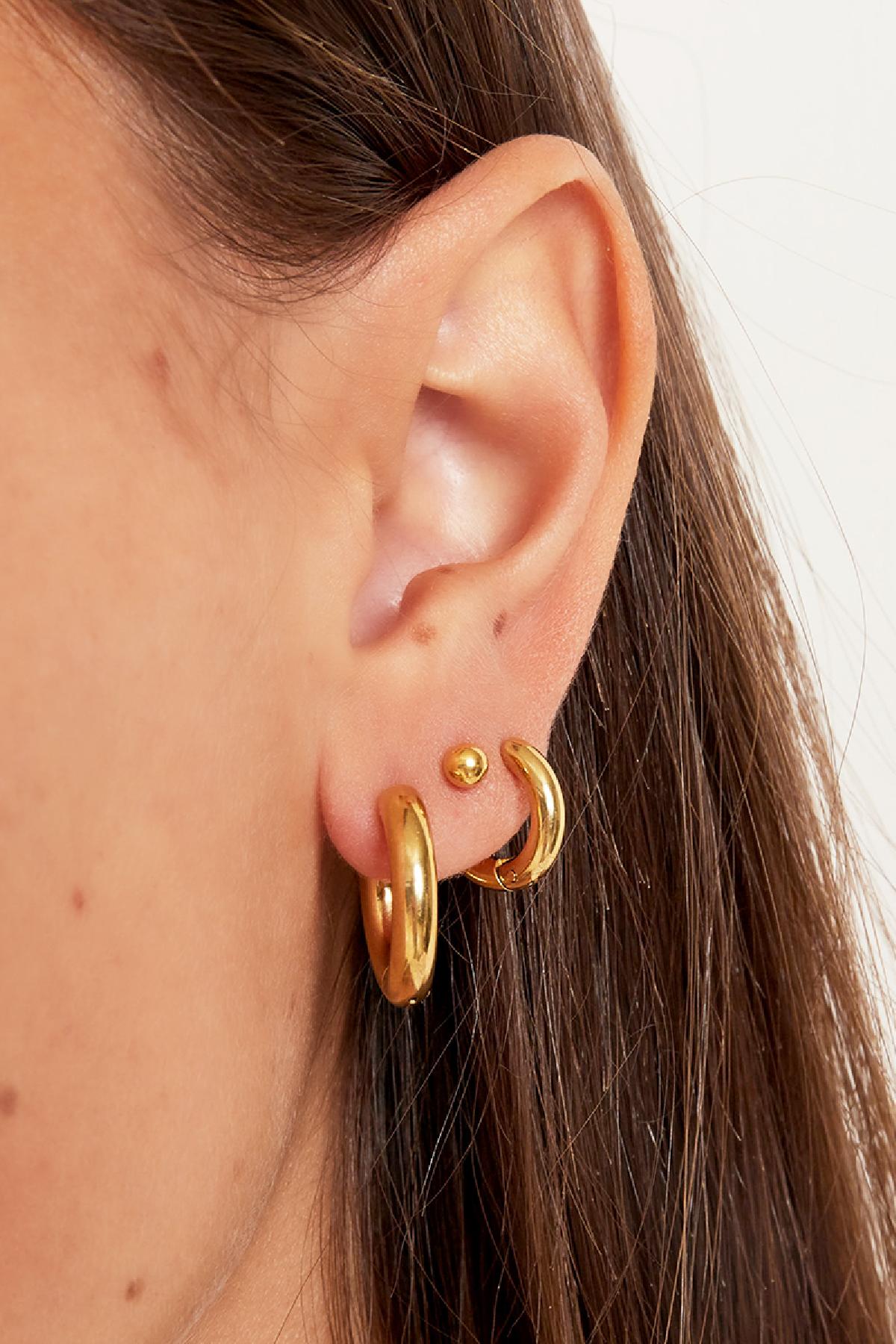 Side view close-up of female ear adorned with stacked chunky gold hoop earrings and a small stud