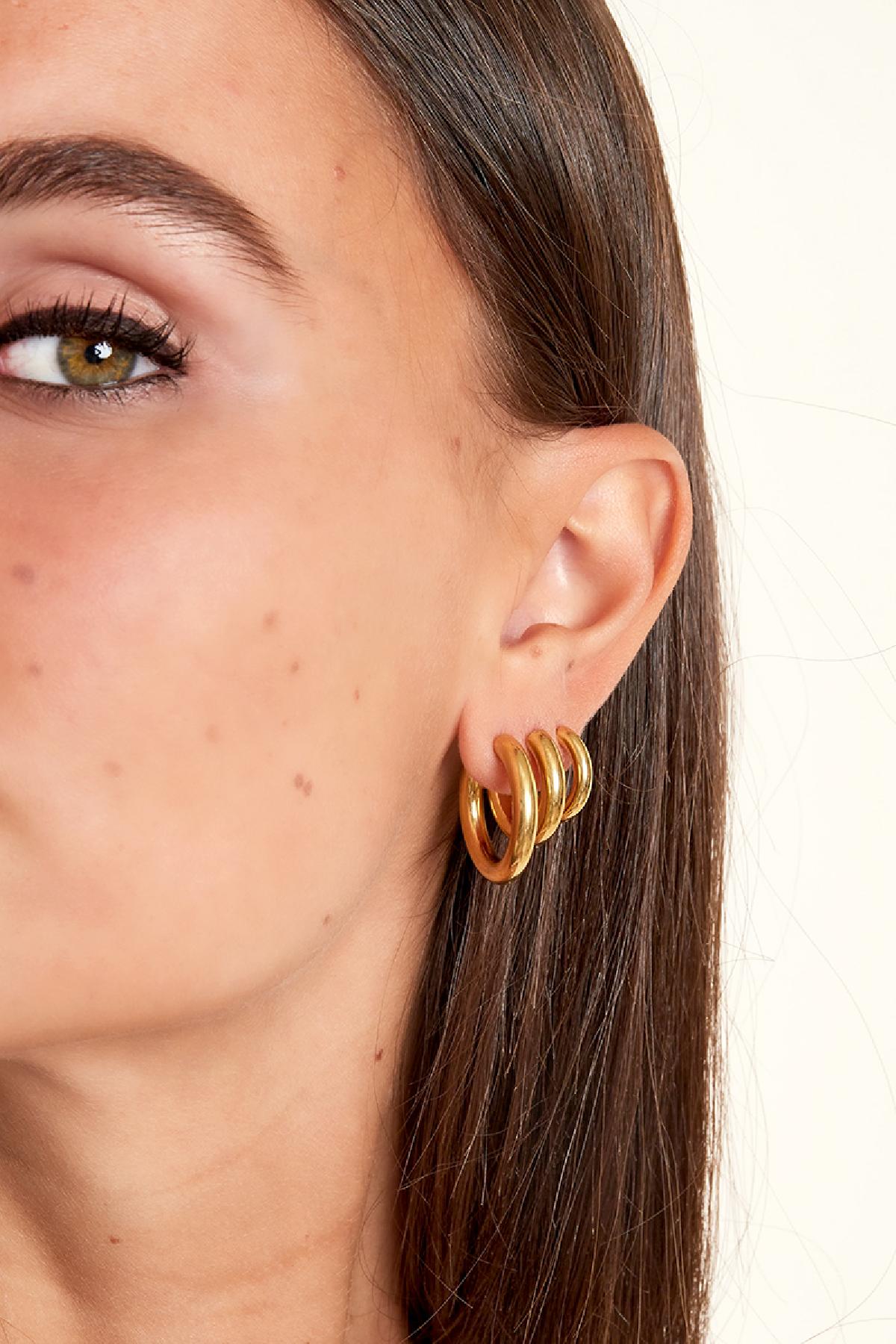 Model wearing multiple chunky gold hoop earrings on one ear showcasing layered styling