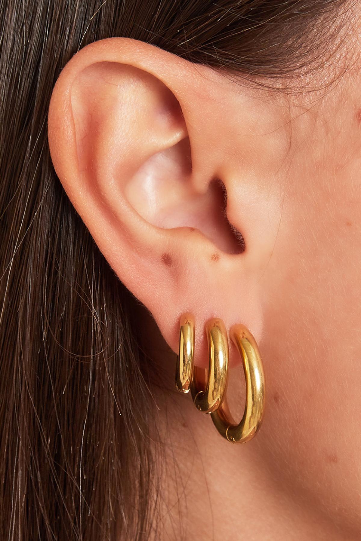 Close-up of an ear wearing three chunky gold hoop earrings with shiny surface