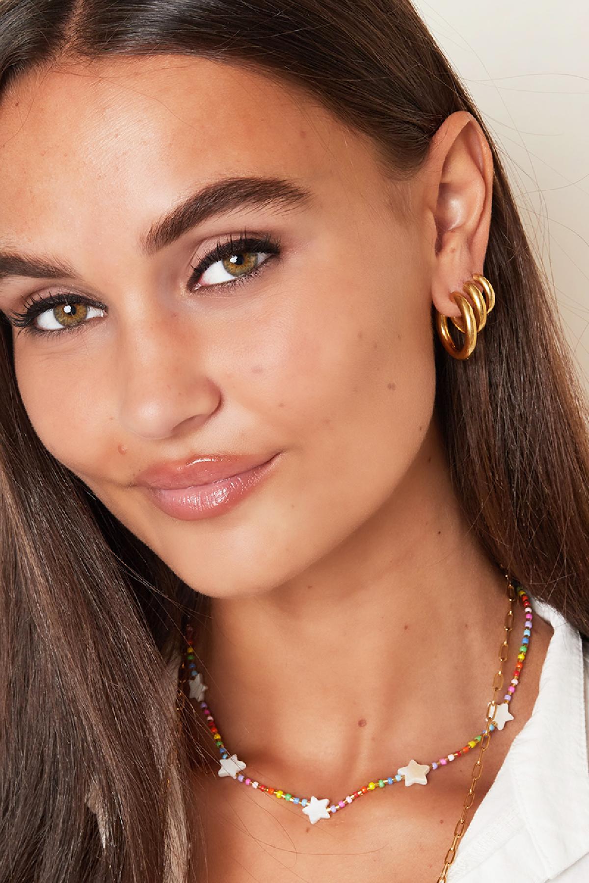 Close-up of woman wearing chunky gold hoop earrings styled with colorful beaded star necklace