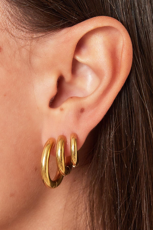 Side view close-up of woman's ear wearing three sizes of chunky gold hoop earrings