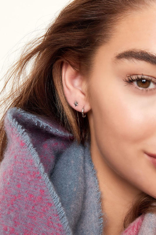 Close-up of ear with small silver star stud and thin silver hoop earring worn with colorful scarf