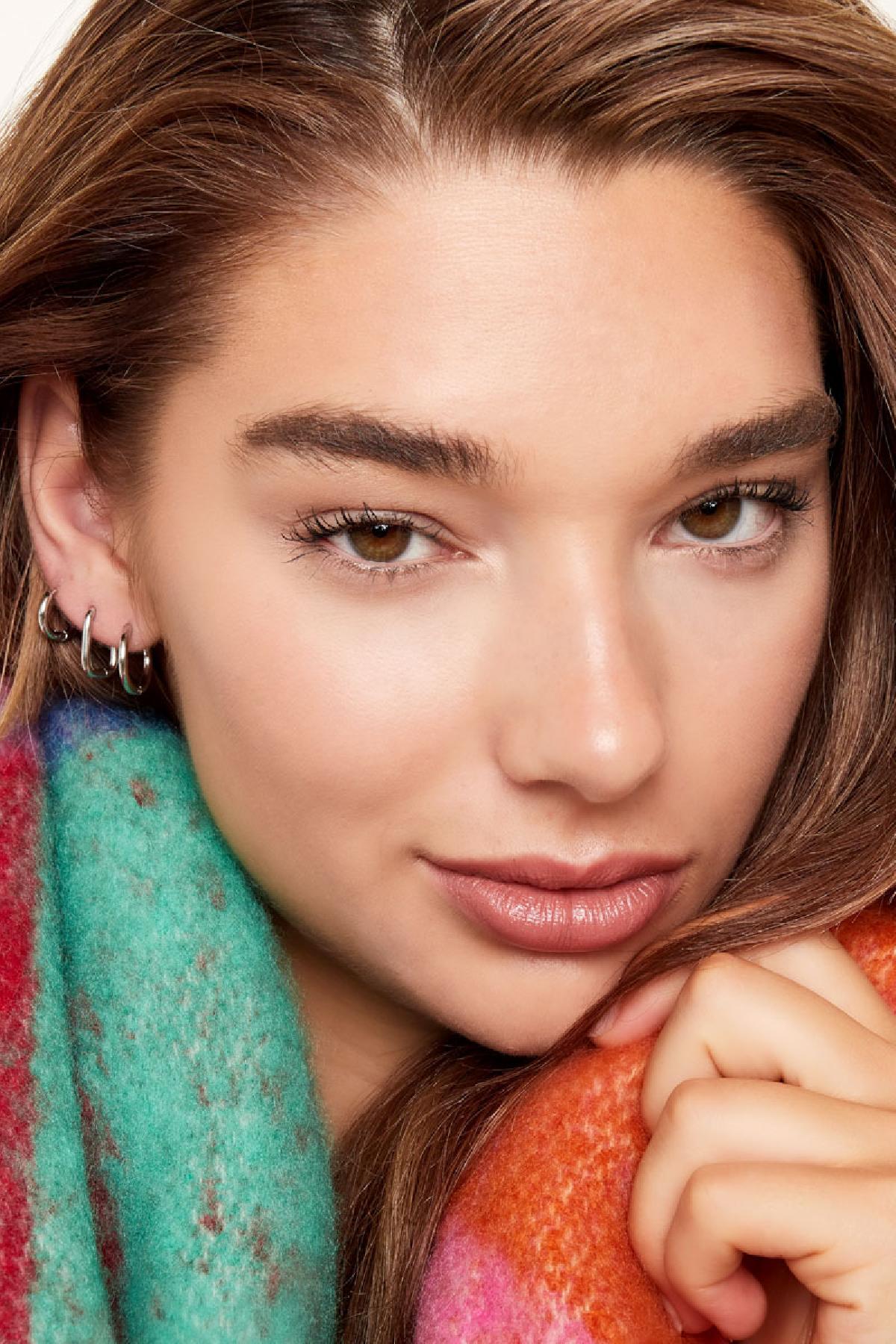 Close-up of ear with multiple small silver hoop earrings worn with colorful cozy scarf