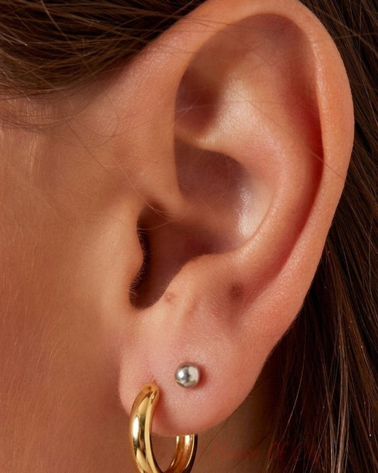 A close-up of a person's ear wearing a polished gold hoop earring and a small silver stud earring.