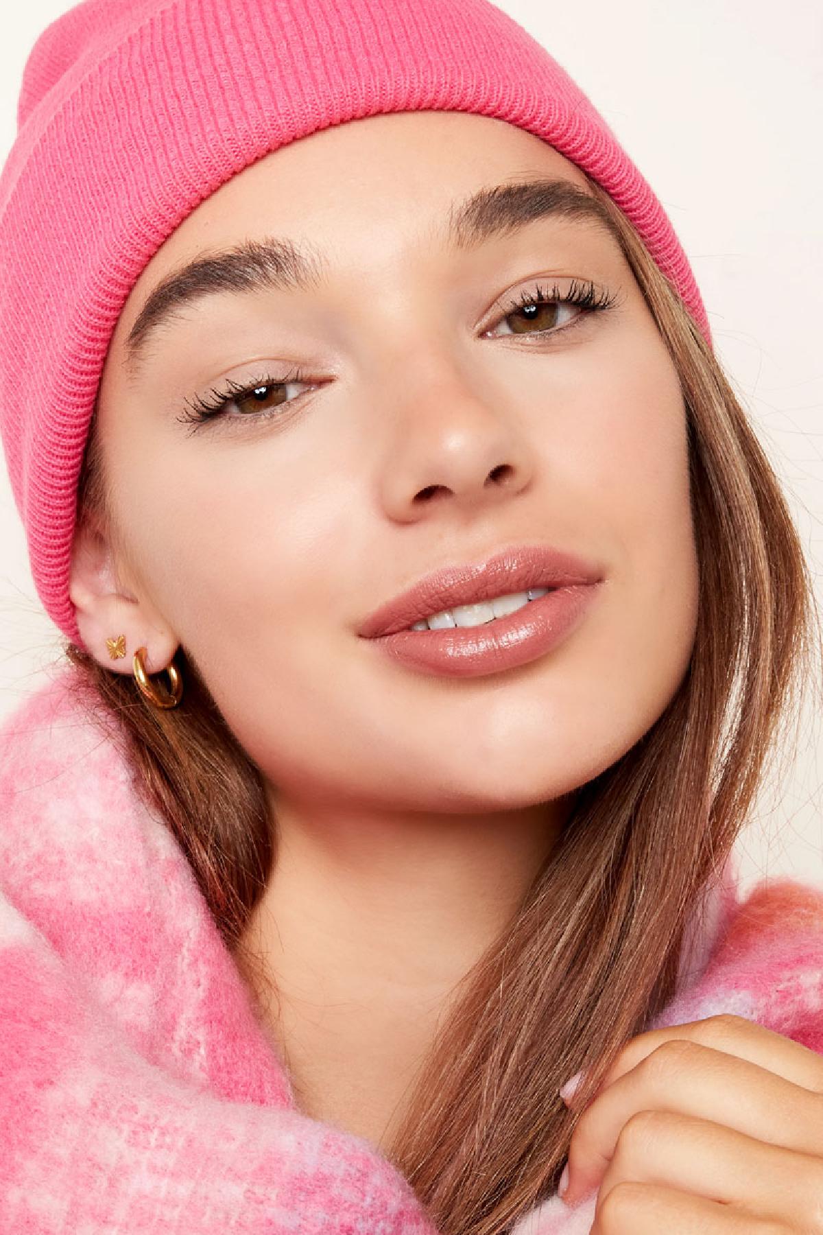 Close-up portrait of a young woman wearing pink beanie and gold hoop earrings with butterfly studs