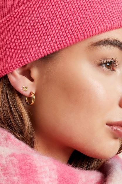 Side close-up of young woman showing gold hoop earrings paired with butterfly stud earrings and pink knitwear