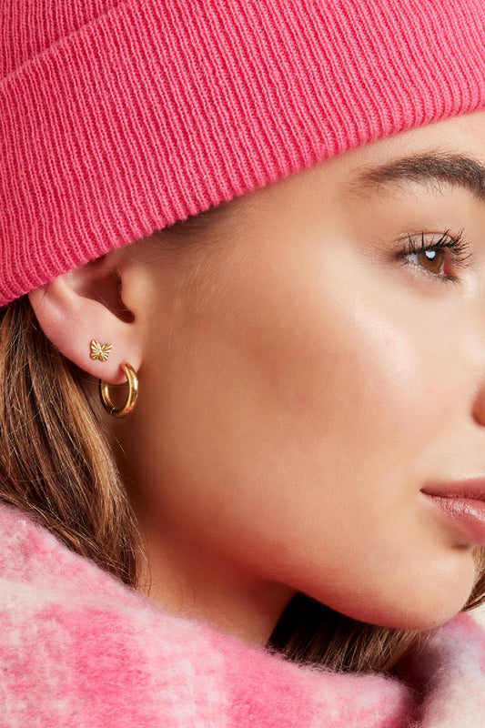 Side close-up of young woman showing gold hoop earrings paired with butterfly stud earrings and pink knitwear