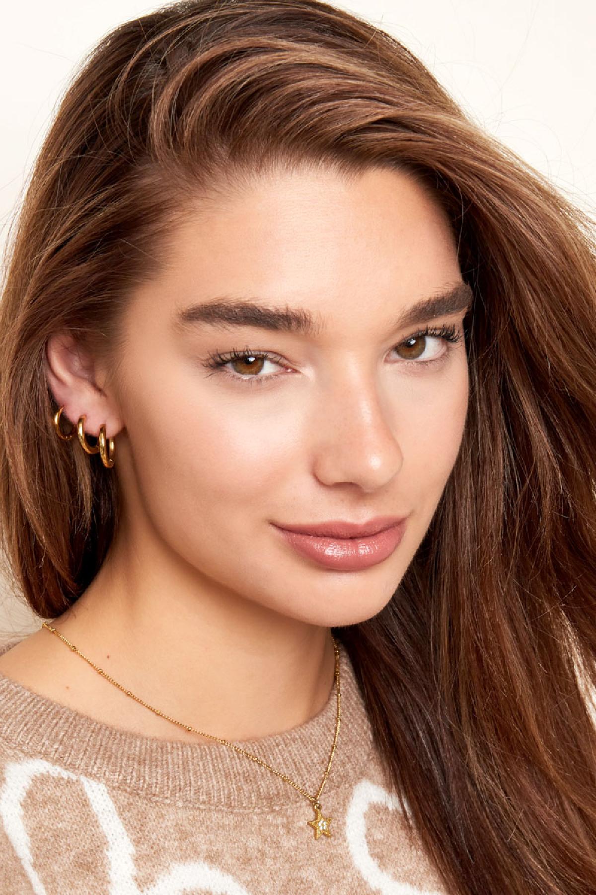 Young woman with three stacked gold hoop earrings showing versatile styling in casual wear and soft natural makeup