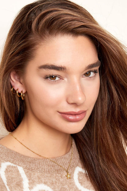 Young woman with three stacked gold hoop earrings showing versatile styling in casual wear and soft natural makeup