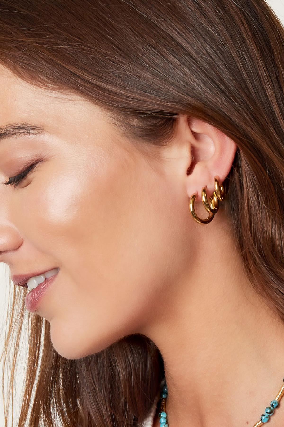 Close-up side profile of a woman wearing three stacked gold hoop earrings with smooth rounded edges