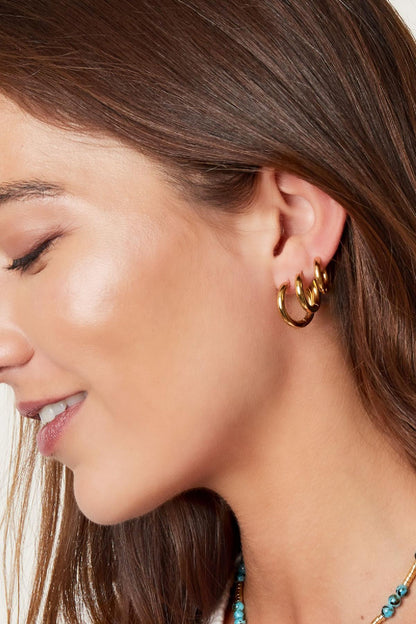 Close-up side profile of a woman wearing three stacked gold hoop earrings with smooth rounded edges
