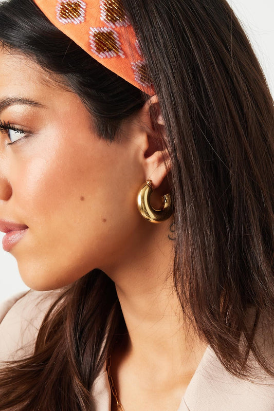 Side profile of woman wearing chunky gold hoop earrings styled with natural makeup and a beige blazer
