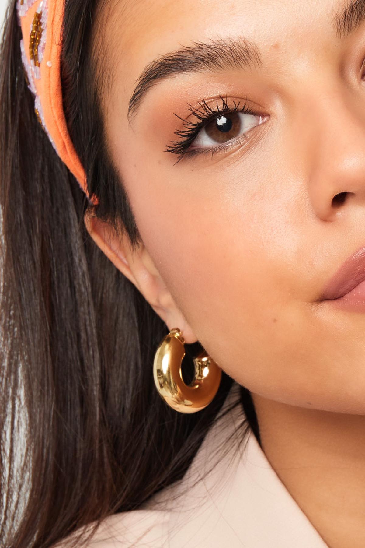 Close-up view of woman wearing chunky gold hoop earring paired with an orange patterned headband