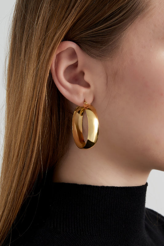 Side view of a woman wearing one wide gold hoop earring paired with a black turtleneck