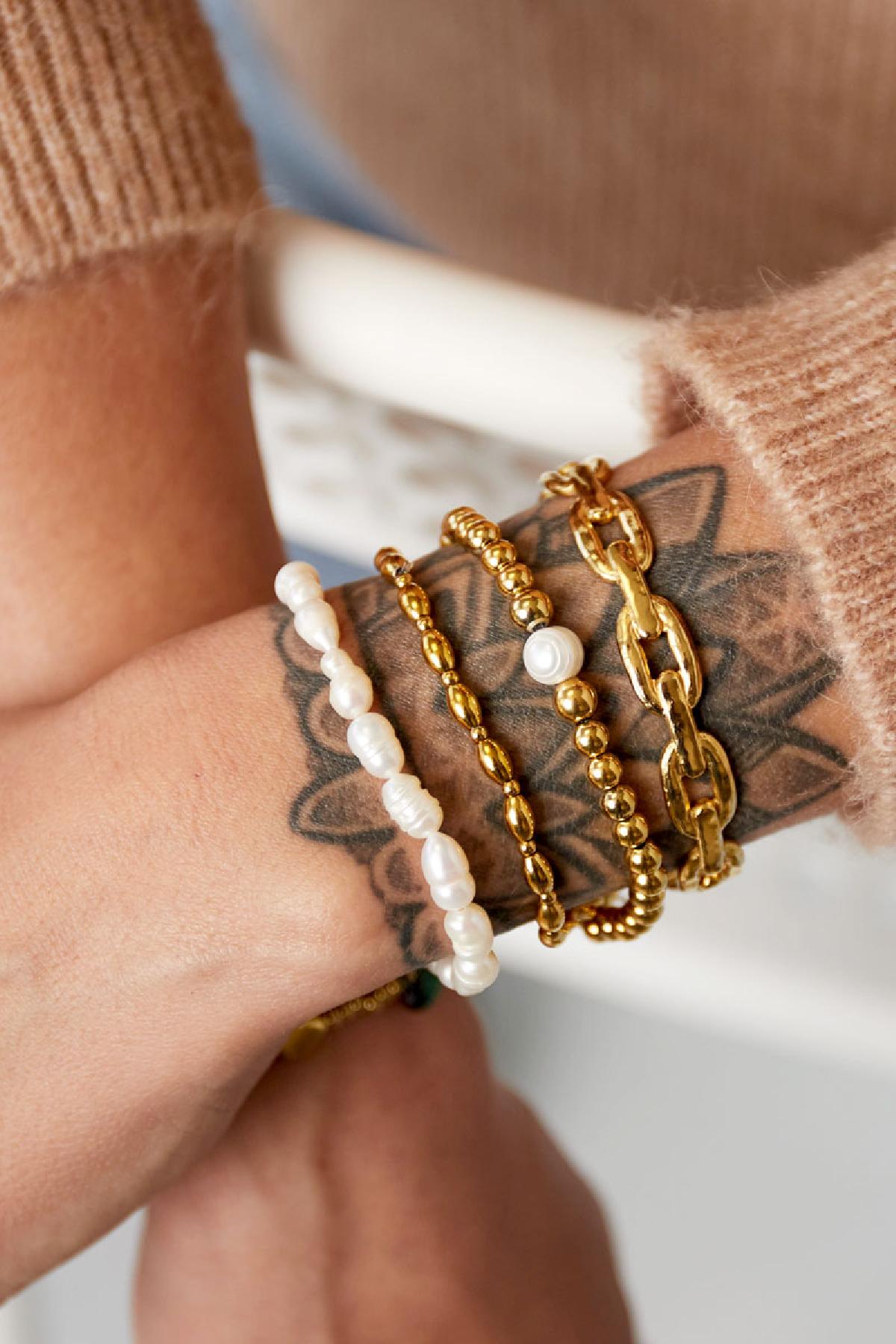 Wrist adorned with layered bracelets including a gold beaded bracelet with pearl, gold chain bracelet, and white pearl bracelet, styled with a cozy sweater