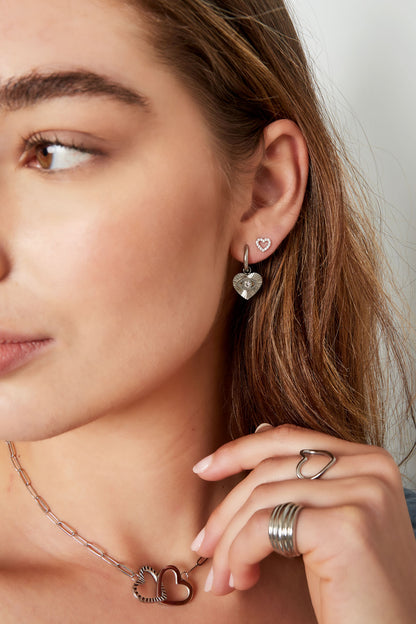 Woman wearing a silver heart pendant necklace, silver eye-heart earrings, silver heart ring, and gold rhinestone heart stud earrings