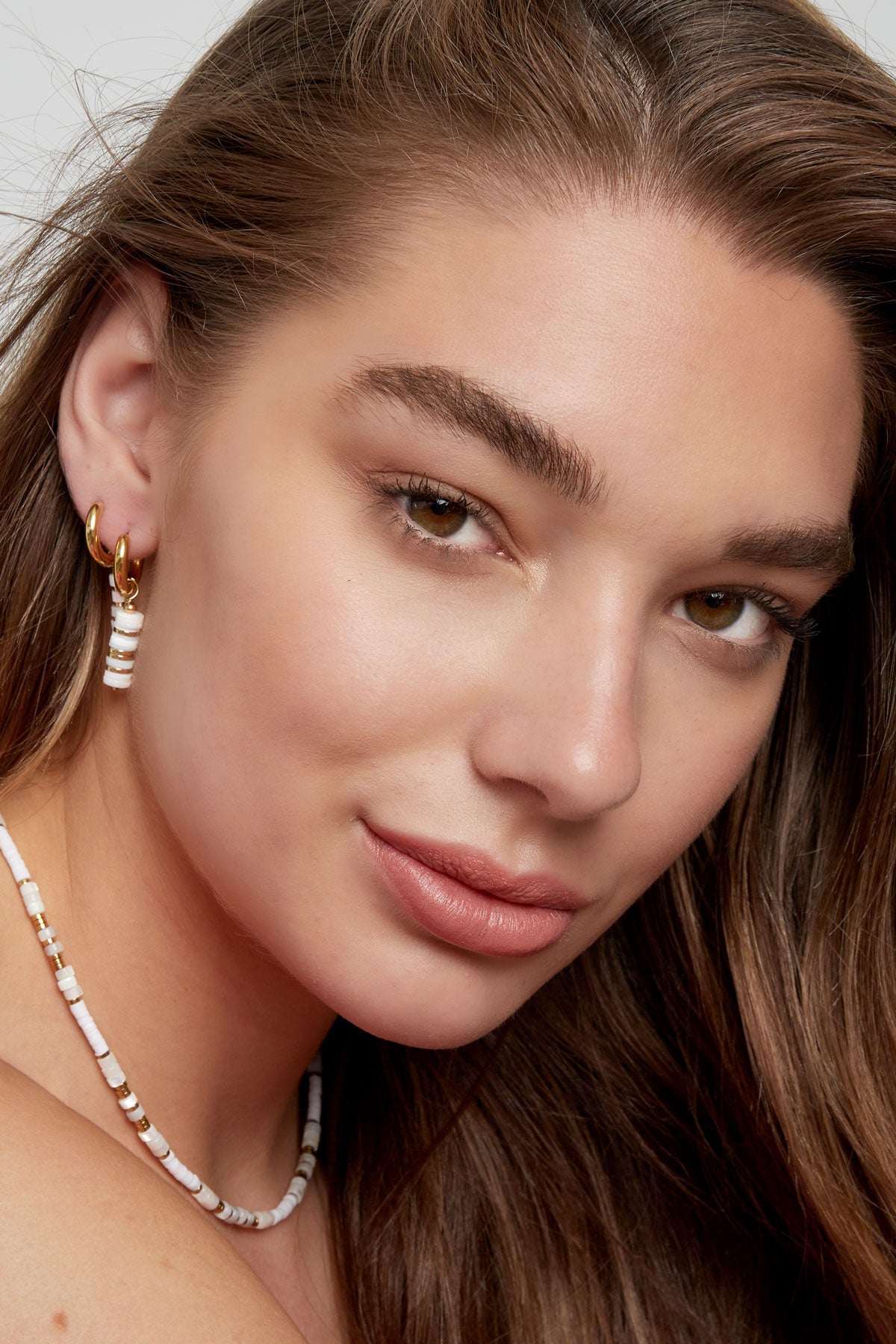 Close-up of a woman wearing gold and white beaded hoop earrings and matching beaded necklace.