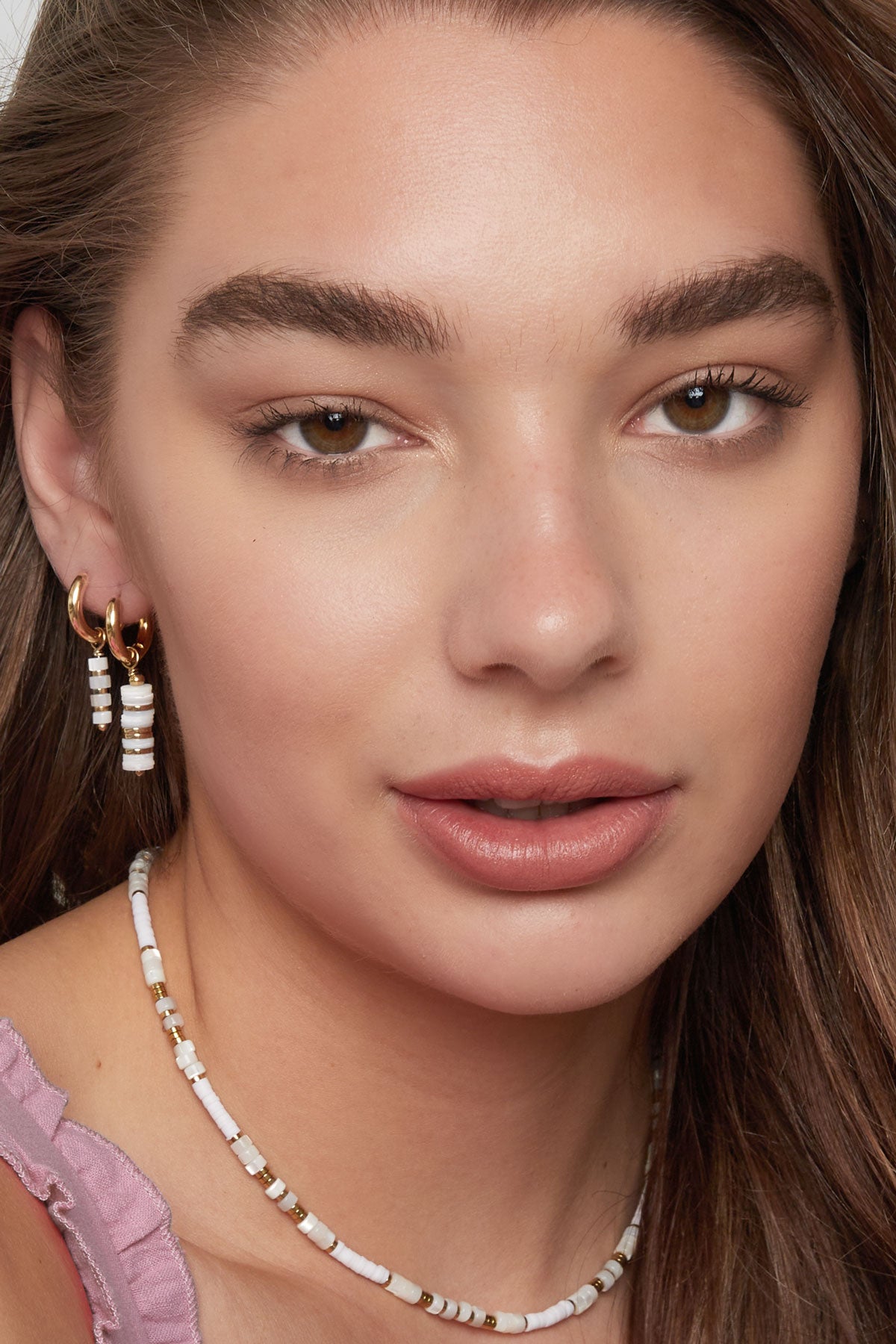 Front view of a woman wearing gold and white beaded hoop earrings and coordinating beaded necklace, showcasing youthful, minimal boutique style.