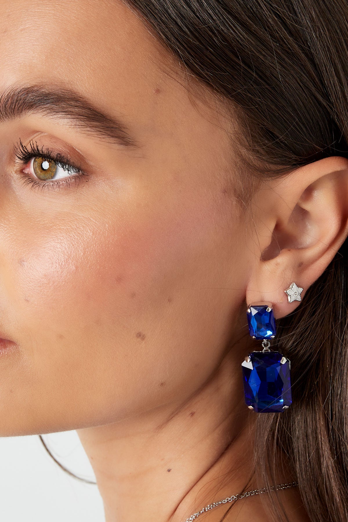 Model close-up showing silver star mini stud earring worn with large blue statement earrings