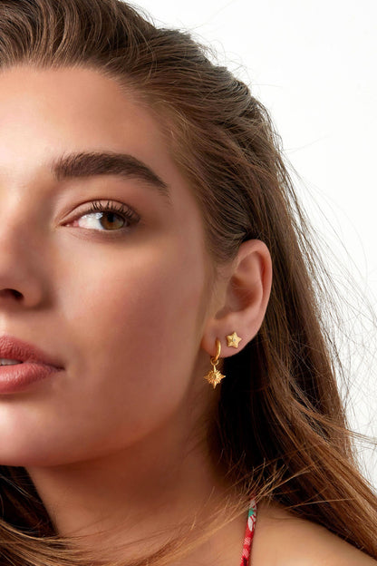 Model wearing gold star mini stud earrings paired with gold hoop earrings against white background