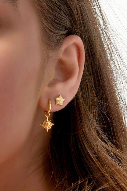 Model close-up showing gold star mini stud earring worn with large blue statement earrings