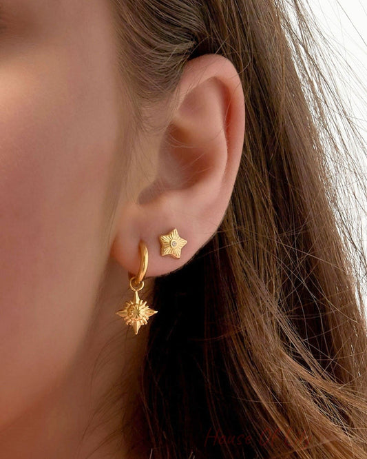 Model close-up showing gold star mini stud earring worn with large blue statement earrings